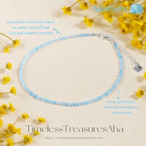 May include: A delicate aquamarine bracelet with a silver clasp and heart charm. The light blue beads are strung together, with text indicating it's a protective stone for travel and brings good luck. The shop name is Timeless TreasuresAha.