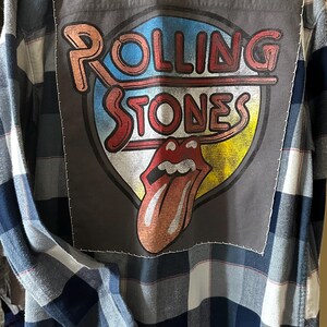 May include: A blue and white plaid flannel shirt with a large Rolling Stones logo patch sewn on the back.