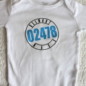May include: White baby onesie with a blue circle graphic that says "BELMONT 02478 MASS".