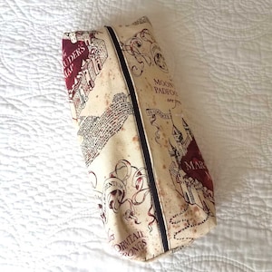 Puede incluir: Una bolsa de cremallera beige con un diseño impreso del Mapa del Merodeador de la serie Harry Potter. El mapa presenta el texto "Marauder's Map" y "Moony, Wormtail, Padfoot, Prongs".