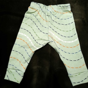 May include: Green baby leggings with a pattern of ants in black, orange, and green marching in a line.