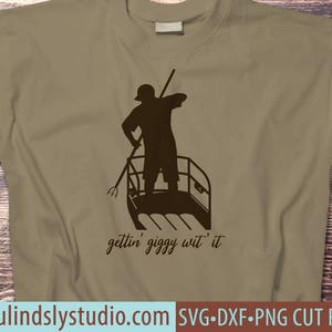 May include: A brown t-shirt with a silhouette of a person rowing a boat. The text "gettin' giggy wit' it" is printed below the image.