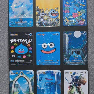 Puede incluir: Nueve cartas coleccionables con personajes de limo azul con varios fondos y texto. Las cartas tienen diferentes diseños, incluyendo paisajes urbanos e ilustraciones de los personajes de limo. Las cartas están en un tarjetero negro.
