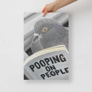 May include: A print featuring a grey pigeon with an orange eye looking over the top of an open book. The book pages are clearly visible, displaying the bold black text that reads POOPING ON PEOPLE in a simple, sans-serif font style.