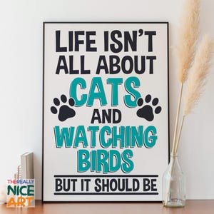 Puede incluir: Una impresión artística enmarcada con el texto "LIFE ISN'T ALL ABOUT CATS AND WATCHING BIRDS BUT IT SHOULD BE" en negro y turquesa. La impresión incluye huellas de patas y se muestra sobre una superficie de madera con un jarrón de plantas secas.