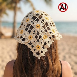 May include: A triangular crochet headscarf featuring a repeating pattern of off-white daisy motifs with bright yellow centers. The accessory is constructed from interconnected floral squares, creating an openwork design that tapers to a point.
