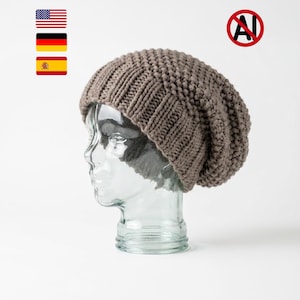 May include: A taupe-coloured knit beanie with a thick ribbed brim and a textured, chunky stitch pattern throughout the crown. The hat is displayed on a clear, transparent mannequin head against a plain, neutral white background.