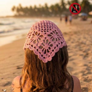 Puede incluir: Un pañuelo de crochet en color rosa empolvado con un motivo floral repetitivo y un patrón de rombos calados. Este accesorio de forma triangular tiene un borde festoneado y está hecho de hilo fino, mostrando un diseño artesanal intrincado.