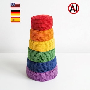 May include: A stack of six cylindrical crochet objects arranged in a vertical tower. The colors from top to bottom are red, orange, yellow, green, blue, and purple. Each piece features a consistent textured stitch pattern throughout the entire stack.