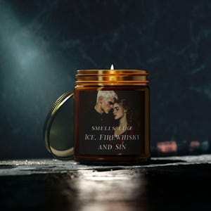 Könnte beinhalten: Ein braunes Glas-Kerzengefäß mit einem goldenen Deckel. Das Gefäß hat ein Etikett mit einem Foto eines sich umarmenden Paares und dem Text "Smells like Ice, Firewhisky and Sin".