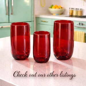 May include: Three red-tinted glass tumblers of varying sizes are arranged on a white countertop. The text "Check out our other listings" is written in cursive at the bottom. The background includes a retro kitchen with a mint green refrigerator.