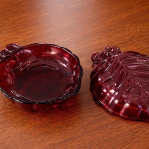 May include: A ruby red glass dish and leaf-shaped lid. The dish has a scalloped edge, and the lid is detailed with leaf veins. The set is made of a transparent, glossy material, likely for decorative use.