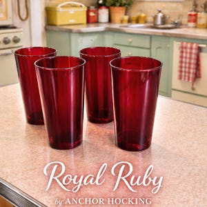 May include: Four ruby red drinking glasses on a countertop. The glasses are tall and cylindrical, with a slightly flared rim. The text "Royal Ruby" and "by ANCHOR HOCKING" are displayed in white script below the glasses.