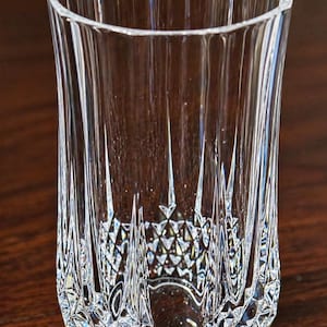 May include: A clear, cut-glass tumbler with a faceted design. The glass features vertical lines along the sides and a diamond-patterned base. The glass is designed for beverages.