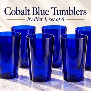 May include: A set of six cobalt blue glass tumblers with a smooth, tapered design. The text Cobalt Blue Tumblers by Pier 1, set of 6 is displayed above the glasses. Each tumbler features a deep, vibrant blue hue and a simple, functional shape.