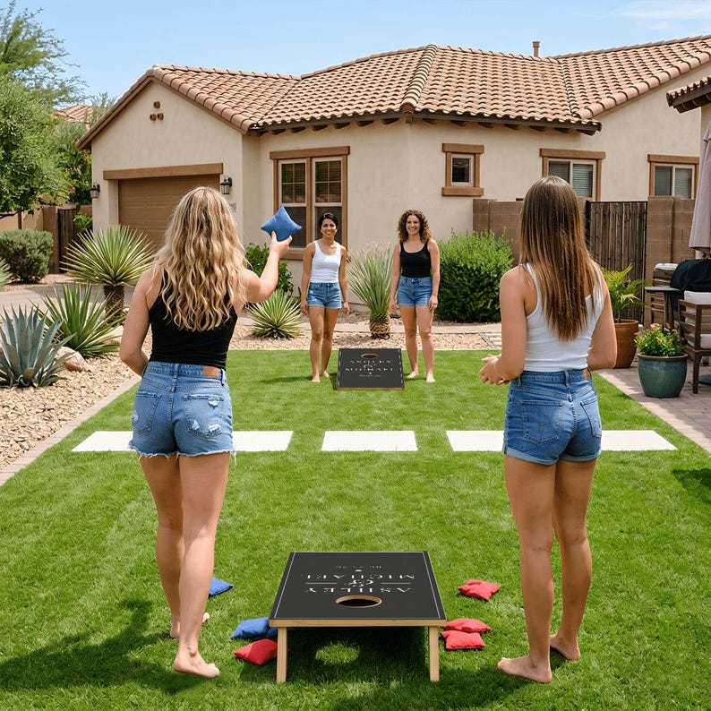 May include: A cornhole game set featuring two black rectangular boards with white text reading Ashley & Michael and a date. The set includes blue and red fabric bean bags. The boards are positioned on a green lawn for outdoor play.