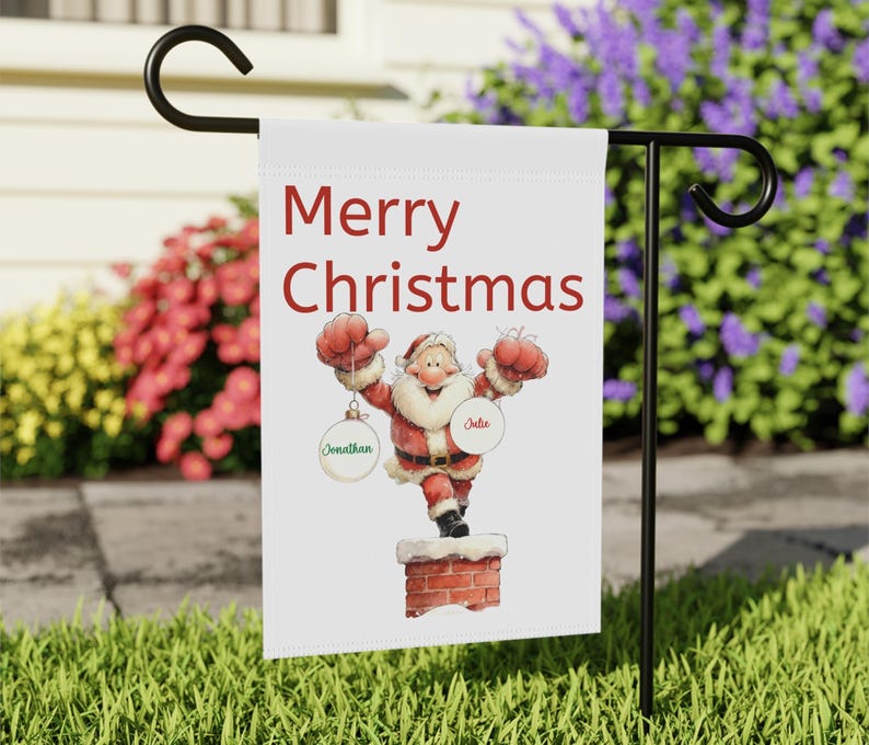 May include: A white garden flag with the words "Merry Christmas" in red. The flag features a cartoon Santa Claus holding ornaments. The ornaments have the names "Jonathan" and "Julie" on them. The flag is displayed on a black metal stand.