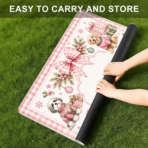 May include: A rectangular mat featuring a white background with a pink gingham border, decorated with illustrations of two dogs in sweaters, gift boxes, holly, and a large pink gingham bow, with the text EASY TO CARRY AND STORE at the top.