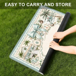 May include: A rolled-up rectangular mat with a detailed, pastel-colored design featuring a beach scene, palm trees, and a large bow. The mat is being rolled up, revealing a black underside. Text at the top reads "EASY TO CARRY AND STORE".