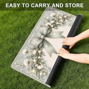 May include: A rectangular mat featuring a festive design with a large grey bow, white cotton flower sprigs, and pine branches on a light background. The text "EASY TO CARRY AND STORE" is printed at the top. The mat has a black underside.