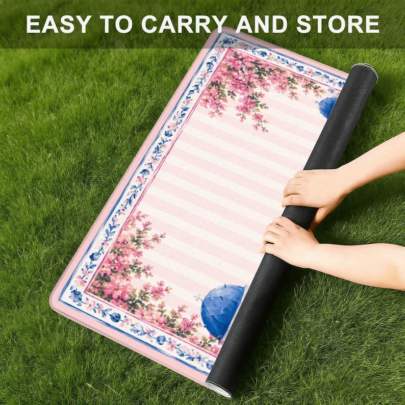 Pode incluir: Um tapete retangular com um centro de riscas rosa claro e brancas, bordado por um padr&atilde;o floral de flores cor-de-rosa e detalhes azuis. O texto EASY TO CARRY AND STORE est&aacute; impresso no topo. O tapete tem uma base preta e cantos arredondados.