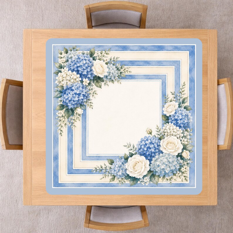 Op de afbeelding: Een vierkante tafelloper met een bloemenontwerp. De loper heeft een lichtblauwe rand met een vierkant kaderontwerp. De hoeken zijn versierd met blauwe hortensia's, witte rozen en groene bladeren. De loper ligt op een houten tafel.