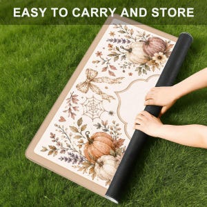 Puede incluir: Una alfombrilla rectangular con borde beige y centro blanco que presenta un dise&ntilde;o impreso de calabazas, hojas de oto&ntilde;o, una telara&ntilde;a y un lazo. El texto EASY TO CARRY AND STORE es visible en la parte superior. La alfombrilla est&aacute; enrollada.