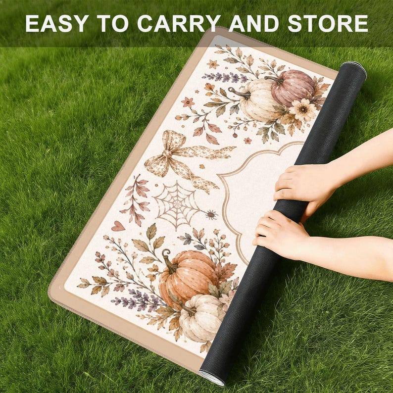 Puede incluir: Una alfombrilla rectangular con borde beige y centro blanco que presenta un dise&ntilde;o impreso de calabazas, hojas de oto&ntilde;o, una telara&ntilde;a y un lazo. El texto EASY TO CARRY AND STORE es visible en la parte superior. La alfombrilla est&aacute; enrollada.