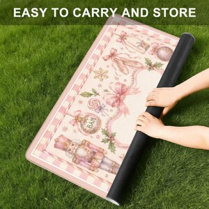 May include: A rolled-up pink and white decorative mat with a black backing, featuring a Christmas-themed design. The mat has a pink and white checkered border and includes images of a nutcracker, ornaments, and bows. The text "EASY TO CARRY AND STORE" is visible.