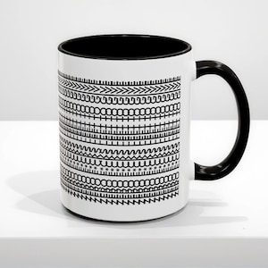 May include: White ceramic mug with a black interior and handle. The exterior has a repeating pattern of black geometric designs. The mug is on a white surface.