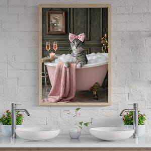 Puede incluir: Un cuadro decorativo enmarcado que muestra a un gato atigrado gris con un lazo rosa claro, sentado en una bañera rosa con patas llena de burbujas blancas. Una toalla rosa cuelga del borde, junto a dos copas de vino rosado y una vela en una mesa.