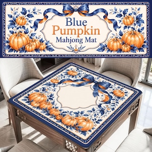 May include: A square mahjong mat featuring a cream-colored center with a blue decorative border. The design includes orange pumpkins, blue leaves, and a blue ribbon bow. The text on the mat reads Blue Pumpkin Mahjong Mat.