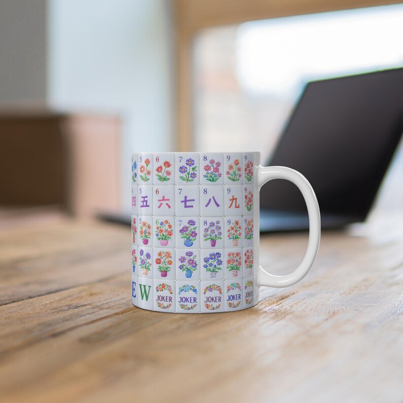 May include: White ceramic mug featuring a design of colorful floral tiles, with numbers and Chinese characters. The mug has a white handle and the word "EW" is printed on the side. The mug is on a wooden surface.