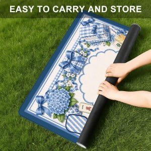May include: A decorative blue and white mat with floral and gift box designs. The mat is rolled up, with the text "EASY TO CARRY AND STORE" at the top. The mat is on a green grassy surface.