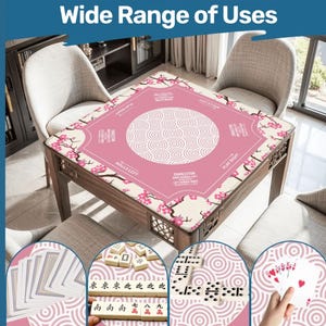 May include: A pink game table cover with a floral design and the text "Wide Range of Uses". The cover features a central circular pattern and is surrounded by decorative cherry blossom branches. The table is made of wood and is surrounded by chairs.