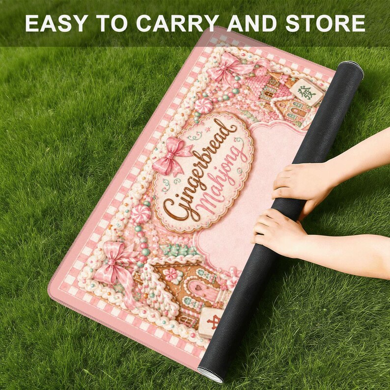 May include: A rectangular mat featuring a pink gingerbread house theme with the text "Gingerbread Mahjong" in a decorative oval frame, accented by pink bows, candy details, and a checkered border, with a black underside and rolled edge.