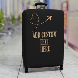 Peut inclure: Housse de valise noire avec un avion et un motif de ligne pointillée en forme de cœur de couleur beige. Le texte "ADD CUSTOM TEXT HERE" est imprimé en beige. La valise a une poignée rétractable et des roues.