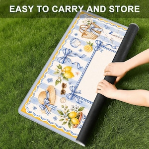 Pu&ograve; includere: Un tappeto rettangolare arrotolato con un design costiero con limoni, un cappello di paglia e fiocchi blu. Il tappeto ha un bordo a righe blu e bianche e il testo "EASY TO CARRY AND STORE" in alto.