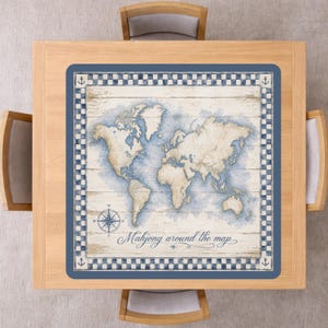 Op de afbeelding: Een vierkante houten tafel met een blauw en wit wereldkaartontwerp. De kaart is omgeven door een blauwe rand met een dambordpatroon en ankericonen. De tekst "Mahjong around the map" staat op de kaart.