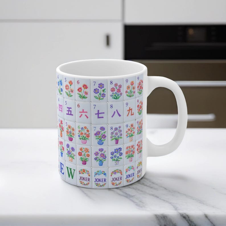May include: White ceramic mug featuring a colorful floral and number design reminiscent of Mahjong tiles. The mug has a curved handle and the word "EW" is printed on the side. The bottom of the mug has the word "JOKER" printed on it.