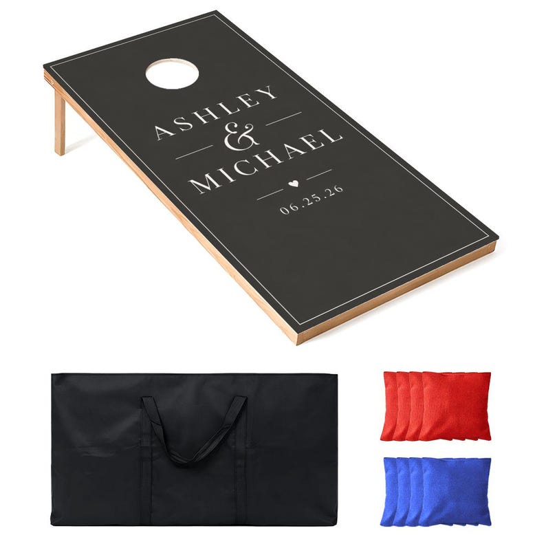 May include: A black cornhole board with a white border, featuring the printed text ASHLEY & MICHAEL, a small heart icon, and the date 06.25.26. The set includes a black carrying bag, four red bean bags, and four blue bean bags for the game.