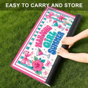 May include: A rolled-up rectangular mat with a pink and white border, featuring the text "MAHJONG GIRL SUMMER" in colorful letters. The mat has a tropical design with cocktails, flowers, and bows. The words "EASY TO CARRY AND STORE" are at the top.