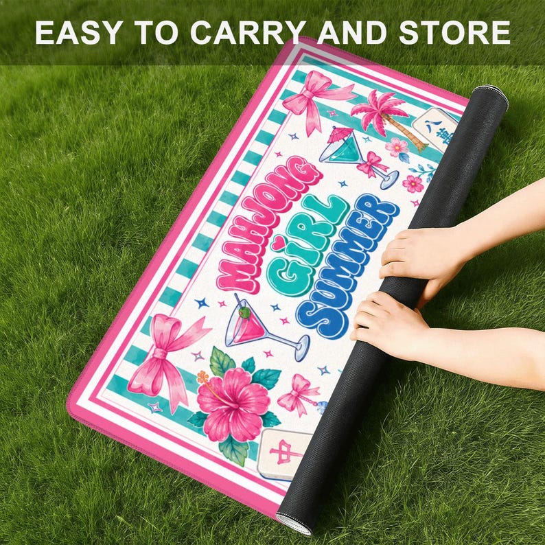May include: A rolled-up rectangular mat with a pink and white border, featuring the text "MAHJONG GIRL SUMMER" in colorful letters. The mat has a tropical design with cocktails, flowers, and bows. The words "EASY TO CARRY AND STORE" are at the top.