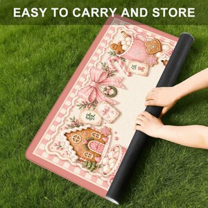 May include: A rolled-up black mat with a pink and white patterned design featuring gingerbread houses, bows, and cookies. The text "EASY TO CARRY AND STORE" is at the top. The mat is on a green grassy surface.