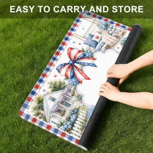 May include: A rectangular mat featuring a red, white, and blue plaid border, a large patriotic bow, and a house illustration with blue flowers. The text "EASY TO CARRY AND STORE" is printed at the top. The mat has a black underside.