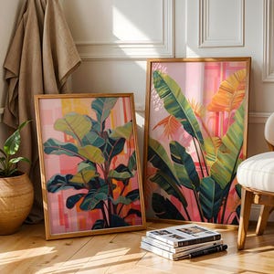May include: Two framed botanical art prints featuring vibrant green and yellow leaves against a pink and orange background. The artwork is displayed in wooden frames, creating a warm and inviting aesthetic. A potted plant and a chair are nearby.