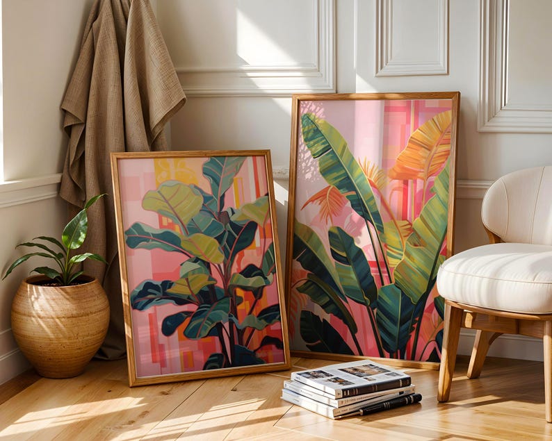 May include: Two framed botanical art prints featuring vibrant green and yellow leaves against a pink and orange background. The artwork is displayed in wooden frames, creating a warm and inviting aesthetic. A potted plant and a chair are nearby.