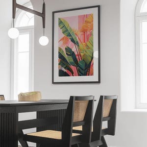 May include: A framed botanical print with a vibrant tropical plant design in shades of green, yellow, and pink. The artwork hangs above a black dining table and chairs with woven backs. The room is illuminated by hanging globe lights.