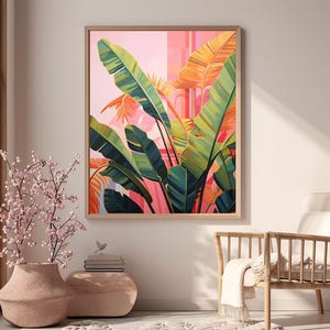 May include: A framed botanical art print featuring large green and yellow banana leaves against a pink and orange background. The artwork is in a wooden frame and hangs on a neutral wall. A vase with pink flowers is in the foreground.