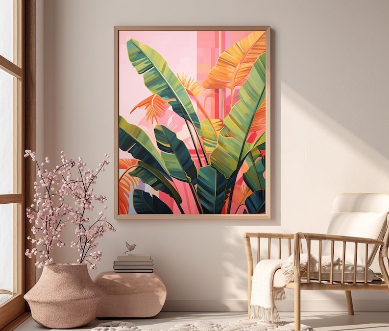 May include: A framed botanical art print featuring large green and yellow banana leaves against a pink and orange background. The artwork is in a wooden frame and hangs on a neutral wall. A vase with pink flowers is in the foreground.